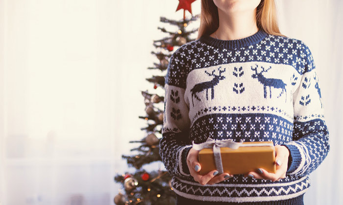 Woman wearing a Christmas jumper and holding a gift