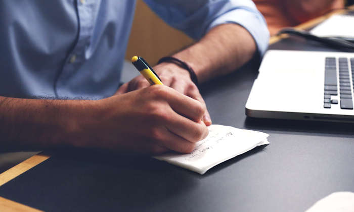 Man writing notes next to a laptop