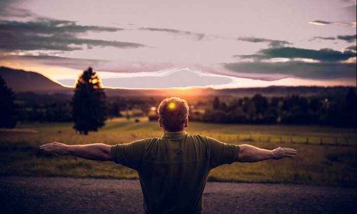 Man with raised arms looking at sunrise