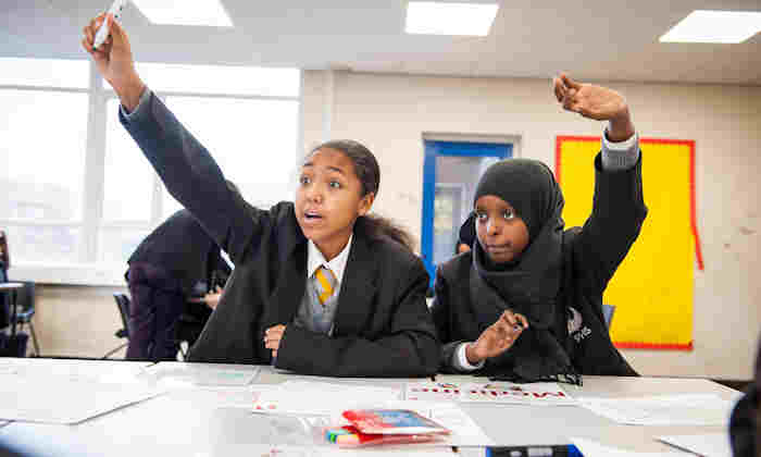 Two school students with hands up in class