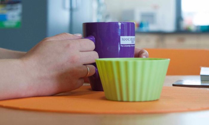 Woman sat at table holding purple University of Manchester mug