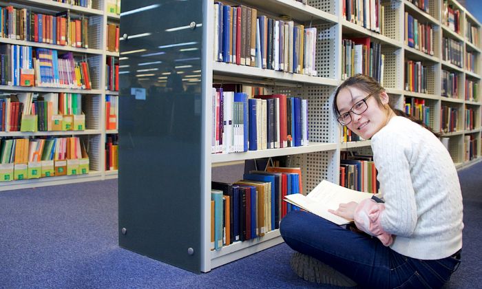 Student sat on the floor in Main Library with a book smiling