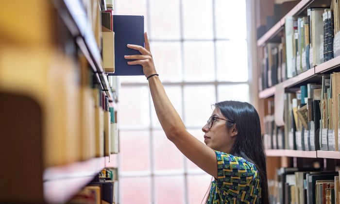 A student reaches up to a shelf to take a book in Main Library