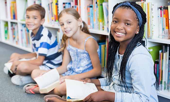 Three smiling children sitting in front of bookshelves