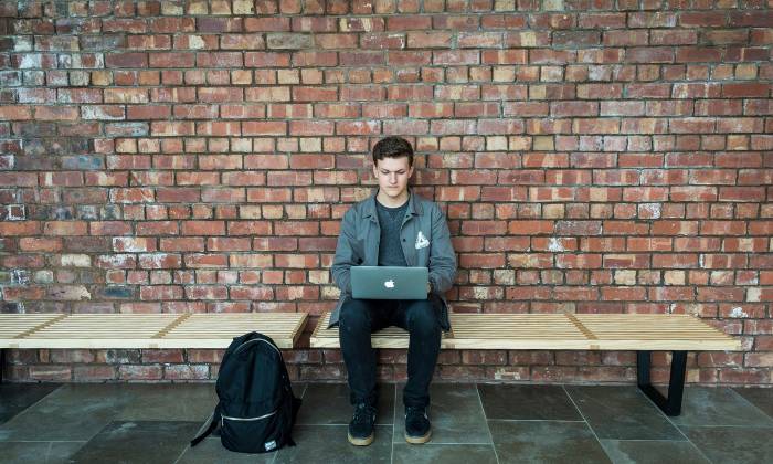 Student sitting against a wall looking at laptop