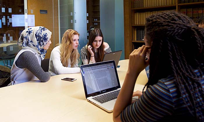 Four students working together at a table with laptops in study room