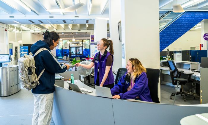 A student is handed a book by two Library Experience staff in Main Library