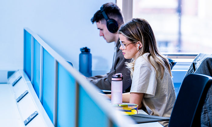 Two students working at desks with laptops in a study area