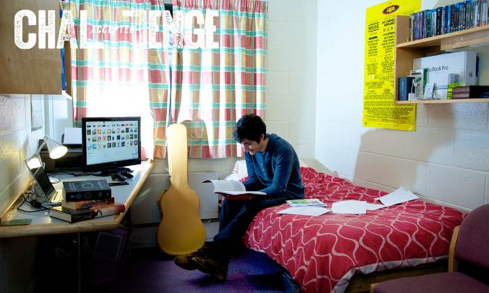 Student sat on his bed, in a university bedroom