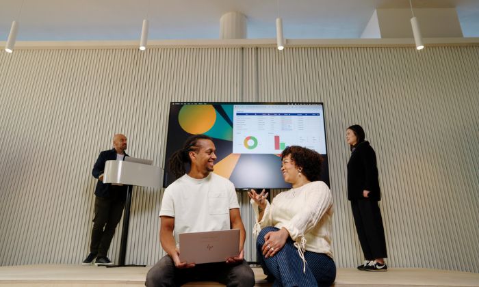 Group of people gathered around a computer with a screen behind